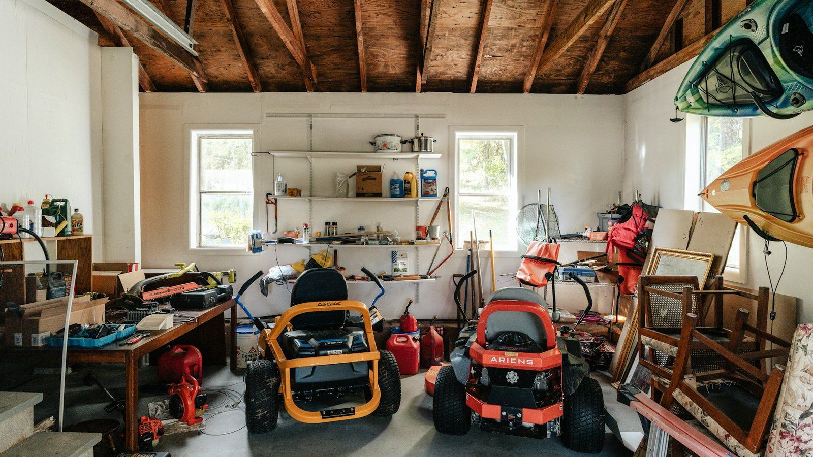 A garage packed with two ride-on mowers, kayaks, stacked picture frames, tools and boxes, with no floor left to walk on