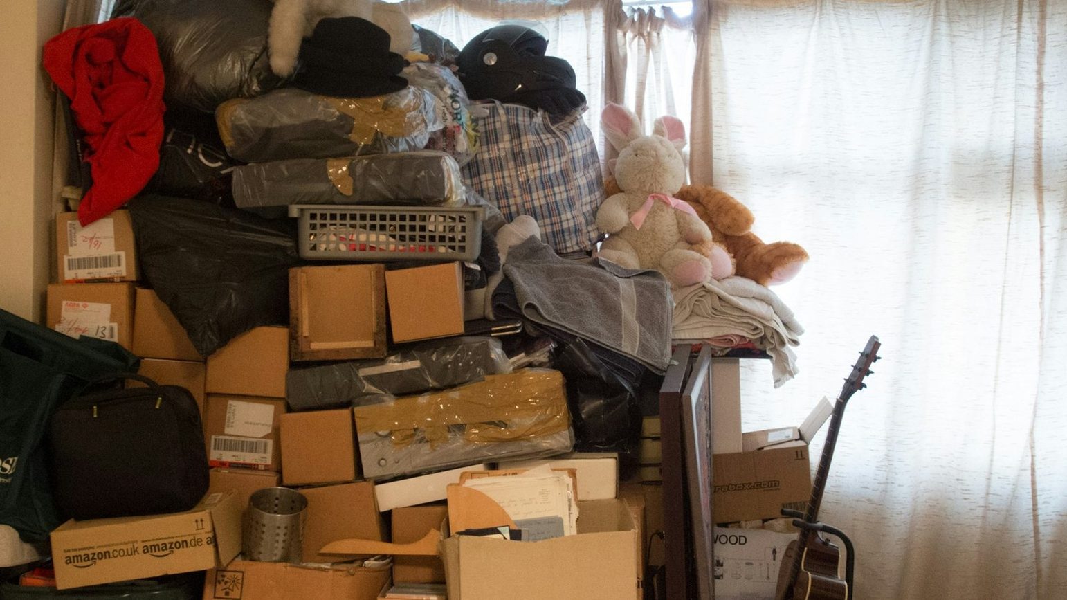 A room stacked to head height with cartons, bagged bedding, soft toys and loose paperwork blocking the window