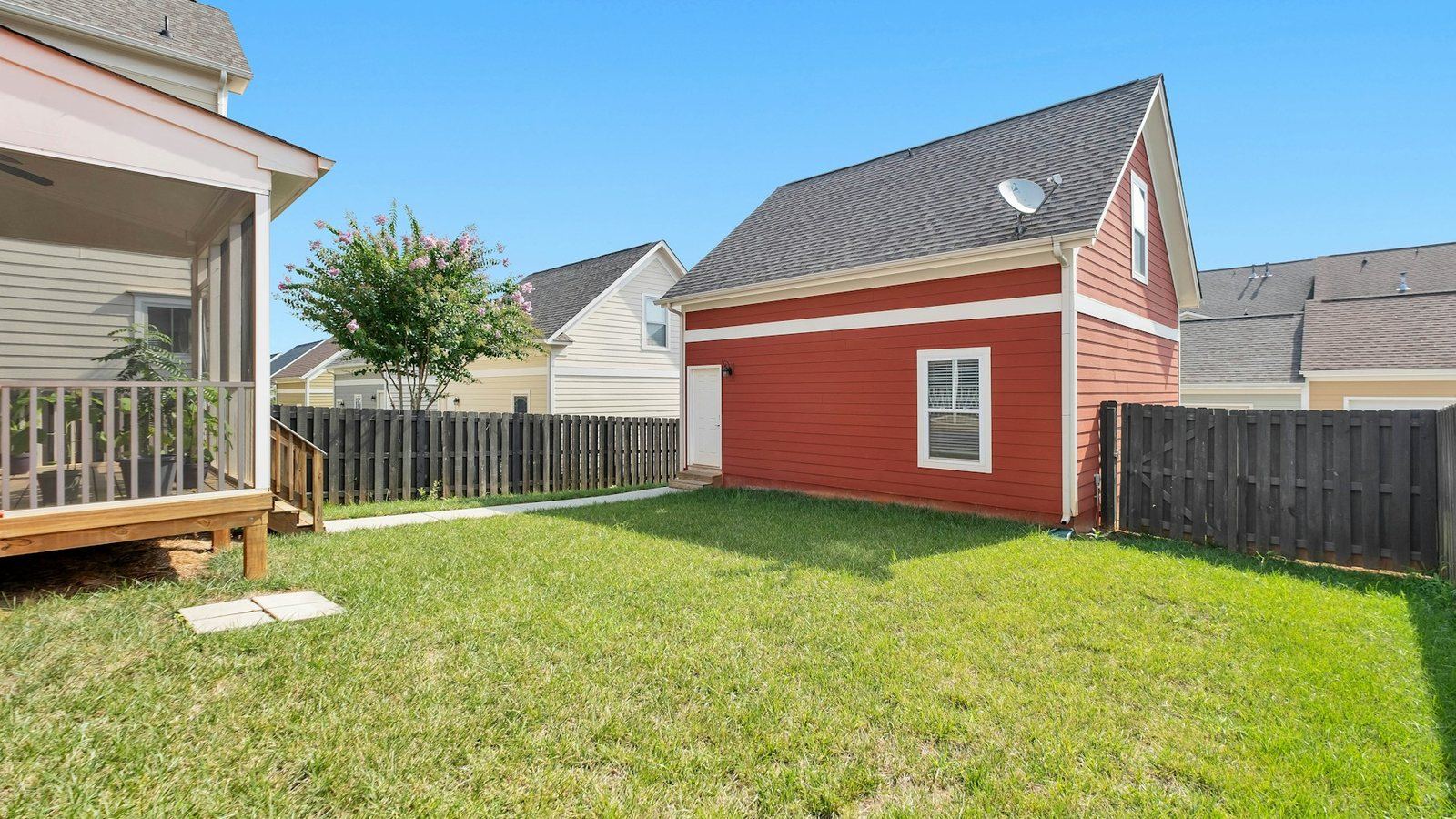 A clear fenced back yard beside a red outbuilding, down to open lawn with nothing stored against the wall