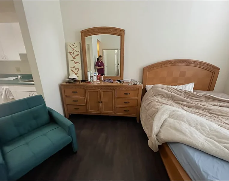 An apartment room with a sofa, dresser and bed left in place before a turnover cleanout