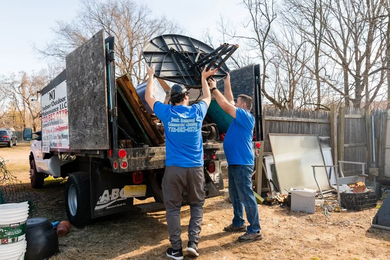 Two NJ Indoor Outdoor crew members lifting a discarded appliance into the truck