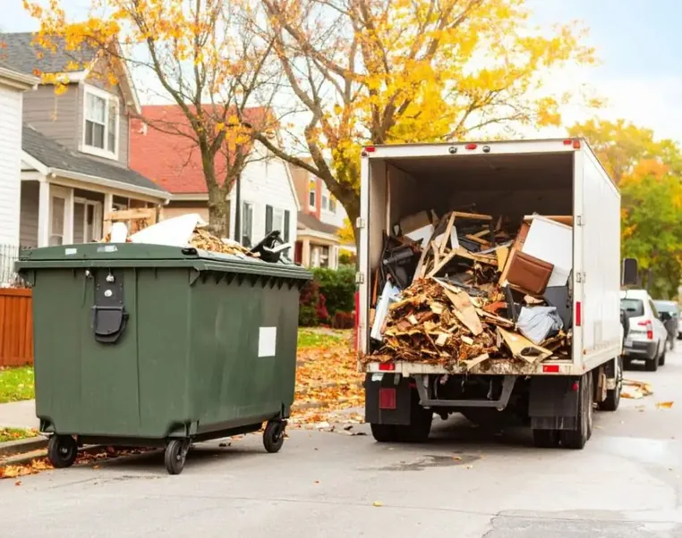 A wheeled dumpster beside a truck loaded with scrap timber on a residential street